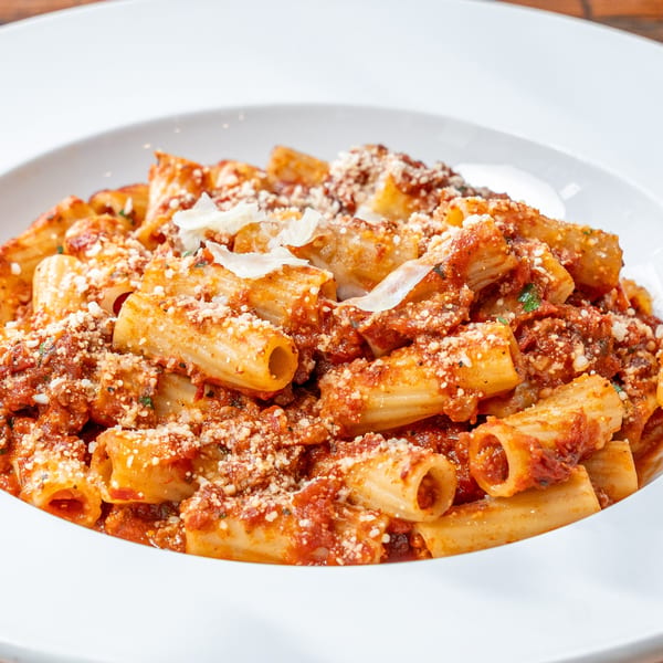 Rigatoni pasta with rich red sauce, grated cheese, and fresh herbs in a white bowl.