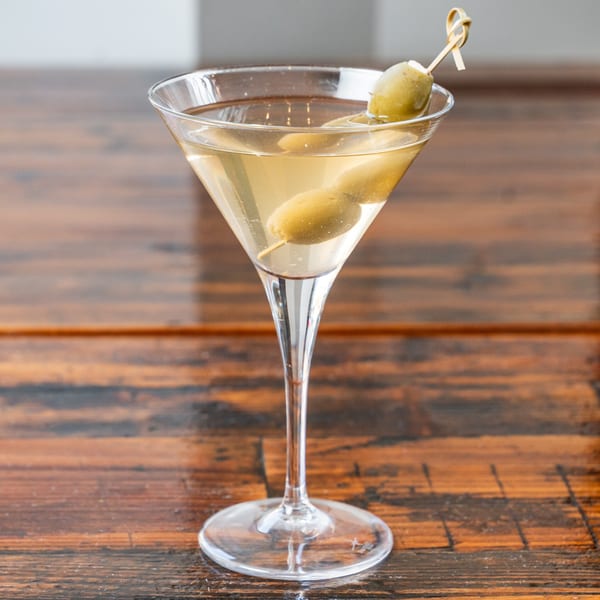 Martini cocktail with three green olives on a skewer, served in a clear glass on a wooden table.