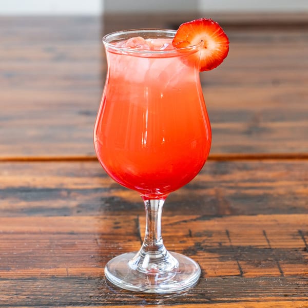 A vibrant red cocktail with ice and a strawberry slice on a rustic wooden table.