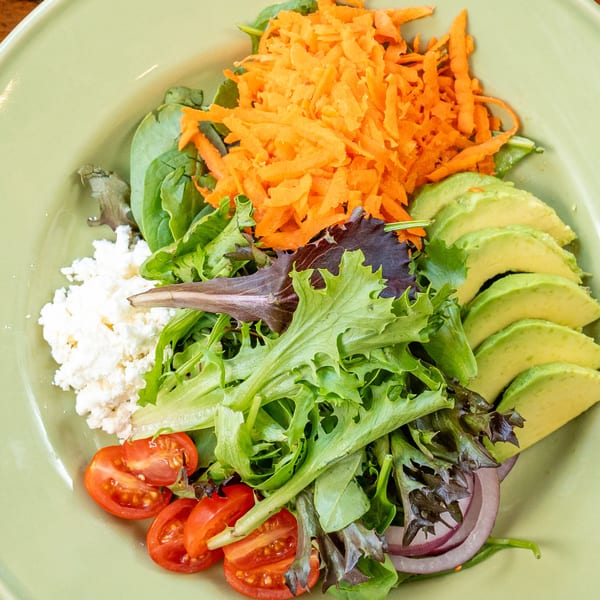 A vibrant Italian salad with mixed greens, shredded carrots, avocado, cherry tomatoes, and feta cheese.