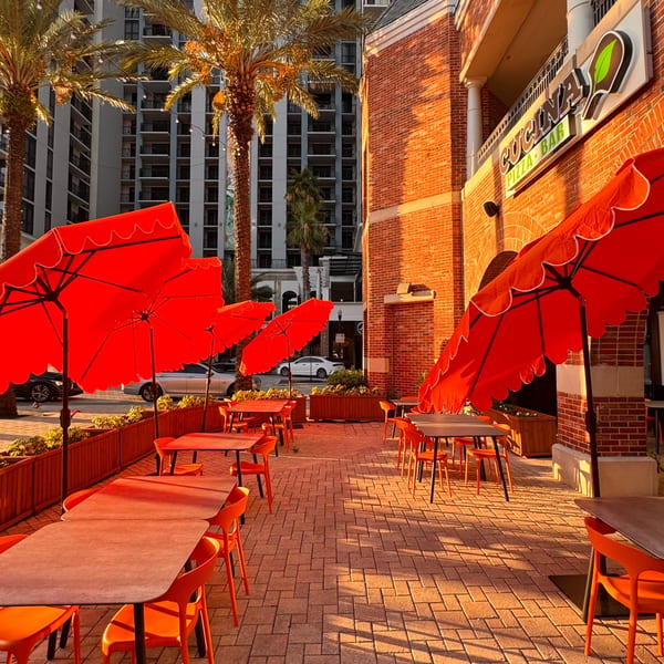 Cucina Pizza & Bar's outdoor patio with orange tables, chairs, and umbrellas under palm trees.