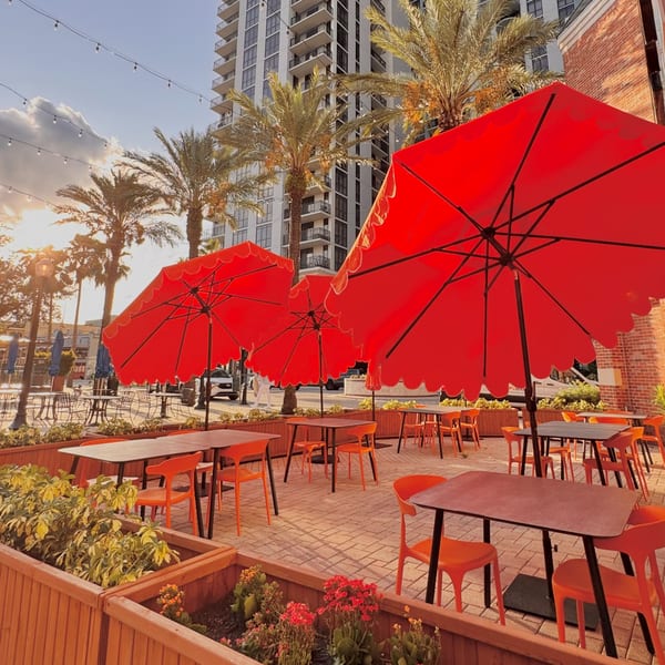 Cucina Pizza & Bar's outdoor patio with red umbrellas, orange chairs, and palm trees.
