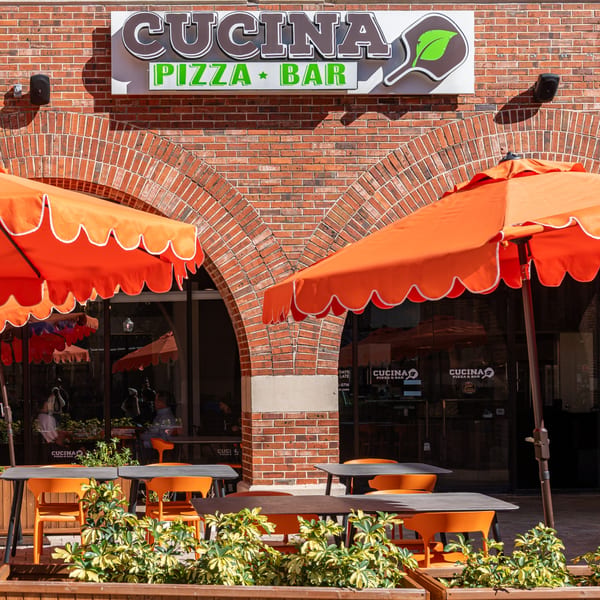 Cucina Pizza & Bar storefront with orange umbrellas, outdoor seating, and a brick facade.