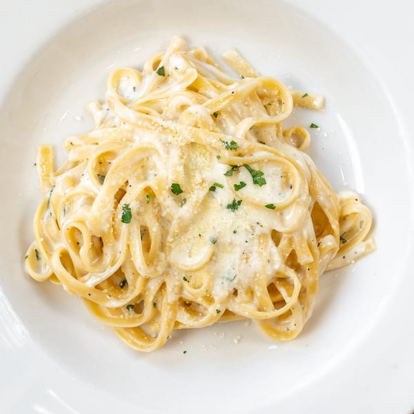 Creamy fettuccine alfredo with parmesan cheese and parsley on a white plate at Cucina Pizza & Bar.